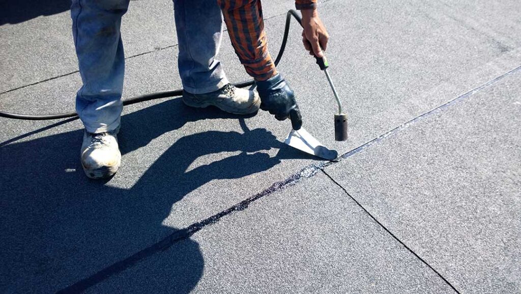Homeowner inspecting a roof from a secured ladder on a dry day with safety gear and tools nearby.